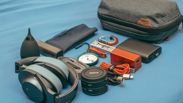 Travel gadgets including headphones, chargers, cables, a power bank, and organizers arranged on a blue surface.