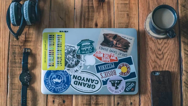 Laptop, headphones, watch, phone, and mug arranged as practical gifts for a 50-year-old man.