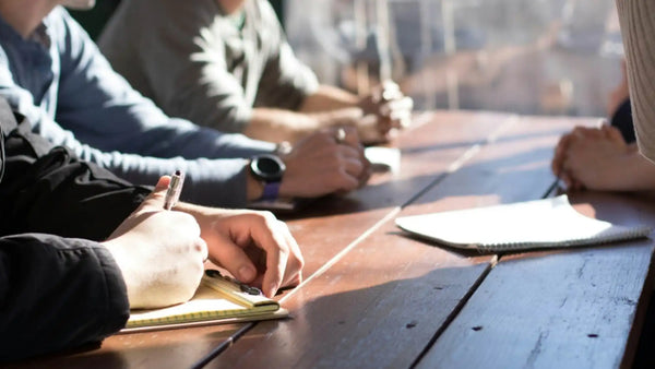 People taking notes around a table during an in-person meeting, a common setting for meeting transcription.